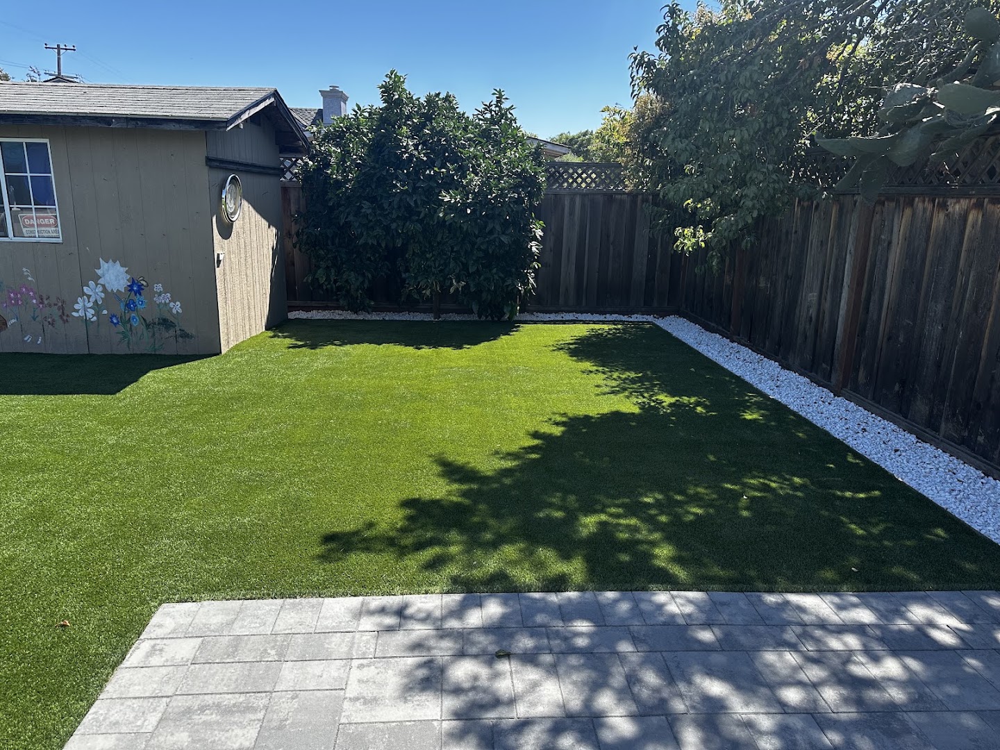 Finished PaveMasters backyard in San Jose with artificial turf, paver patio, and white rock borders